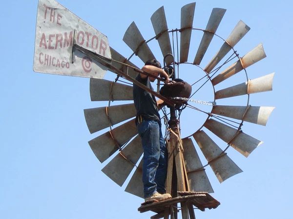 Large windmill turbine spinning in a green field under blue sky, symbolizing sustainable wind renewable energy on the home page